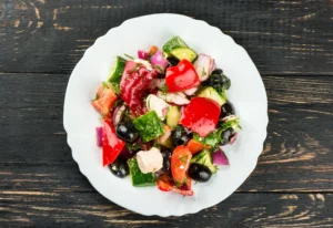 A white plate topped with salad on top of wooden table.