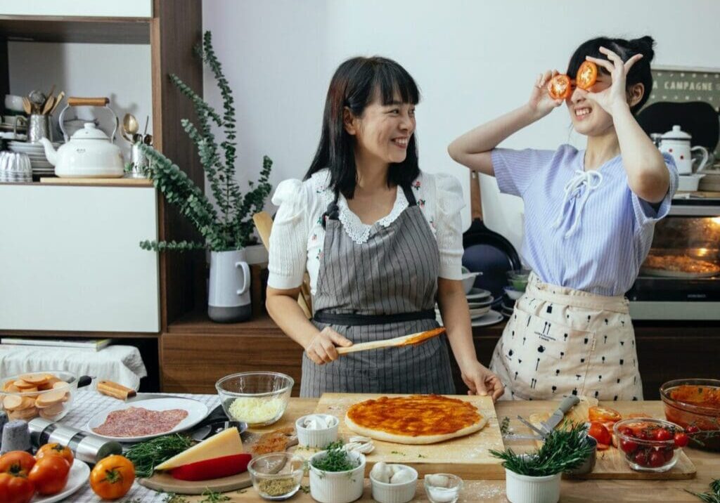 Two women standing in front of a table with food.